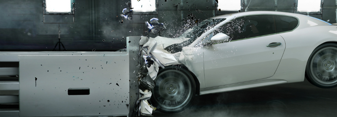 White vehicle slams into a metal barrier in some kind of crash test in a factory.