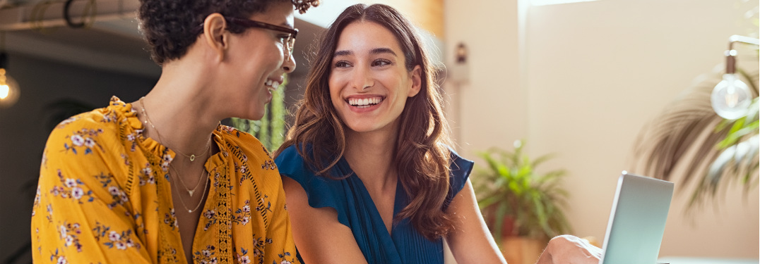 Two women smile as they enjoy a computer.