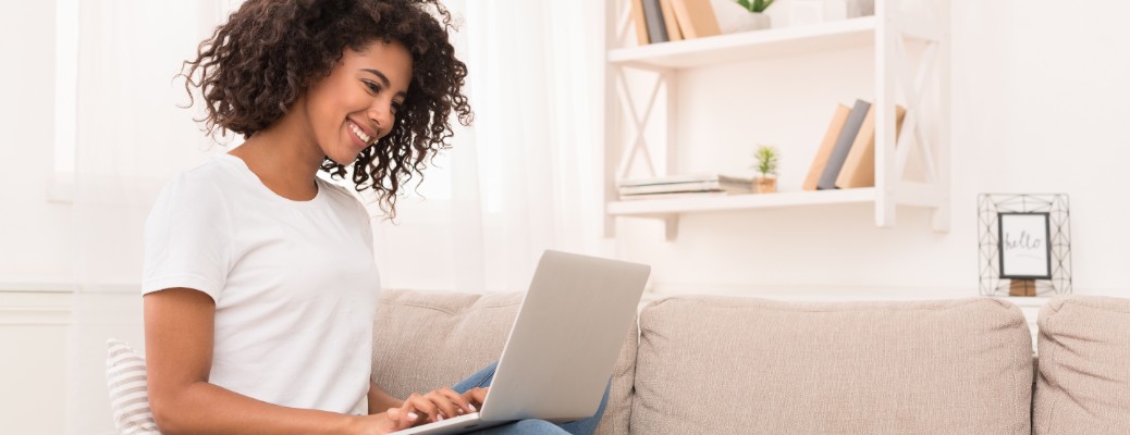 Young African-American woman sitting on a couch on her laptop and smiling.