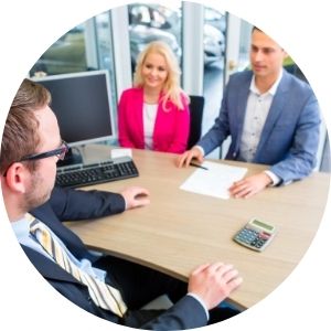 Car Salesman Sitting at a Desk with a Couple Signing Paperwork