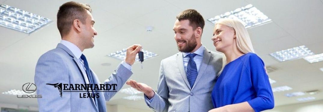 Car Salesman Handing Keys to Young Couple in a Dealership with Earnhardt Lexus Logo in Lower Left