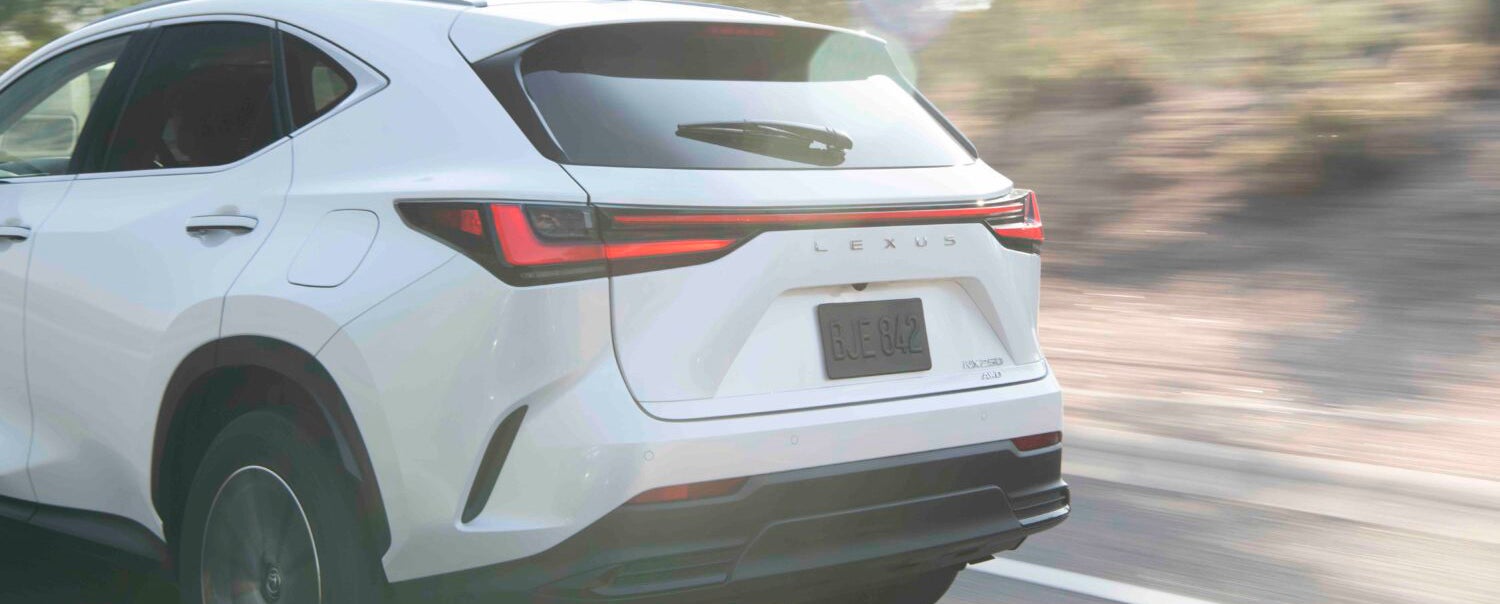 A white Lexus NX 350h SUV driving on a road, seen from the rear with its taillights illuminated.