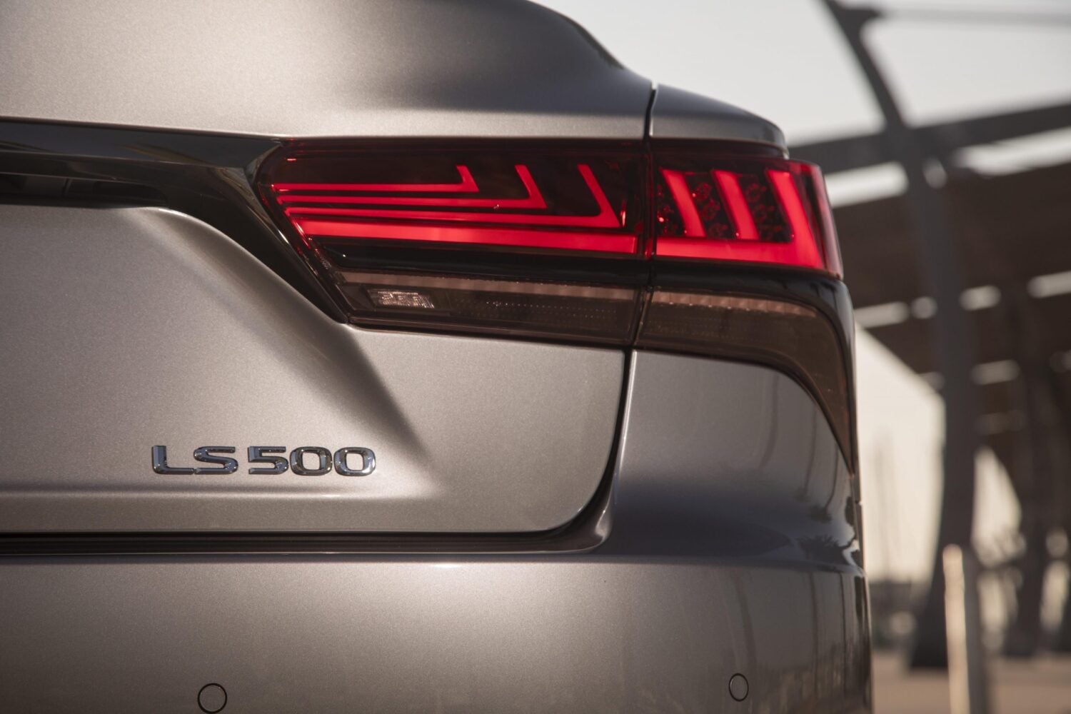 The right side of the back of a grey 2026 Lexus Luxury Sedan is seen up close with the name "LS 500" in silver letters.