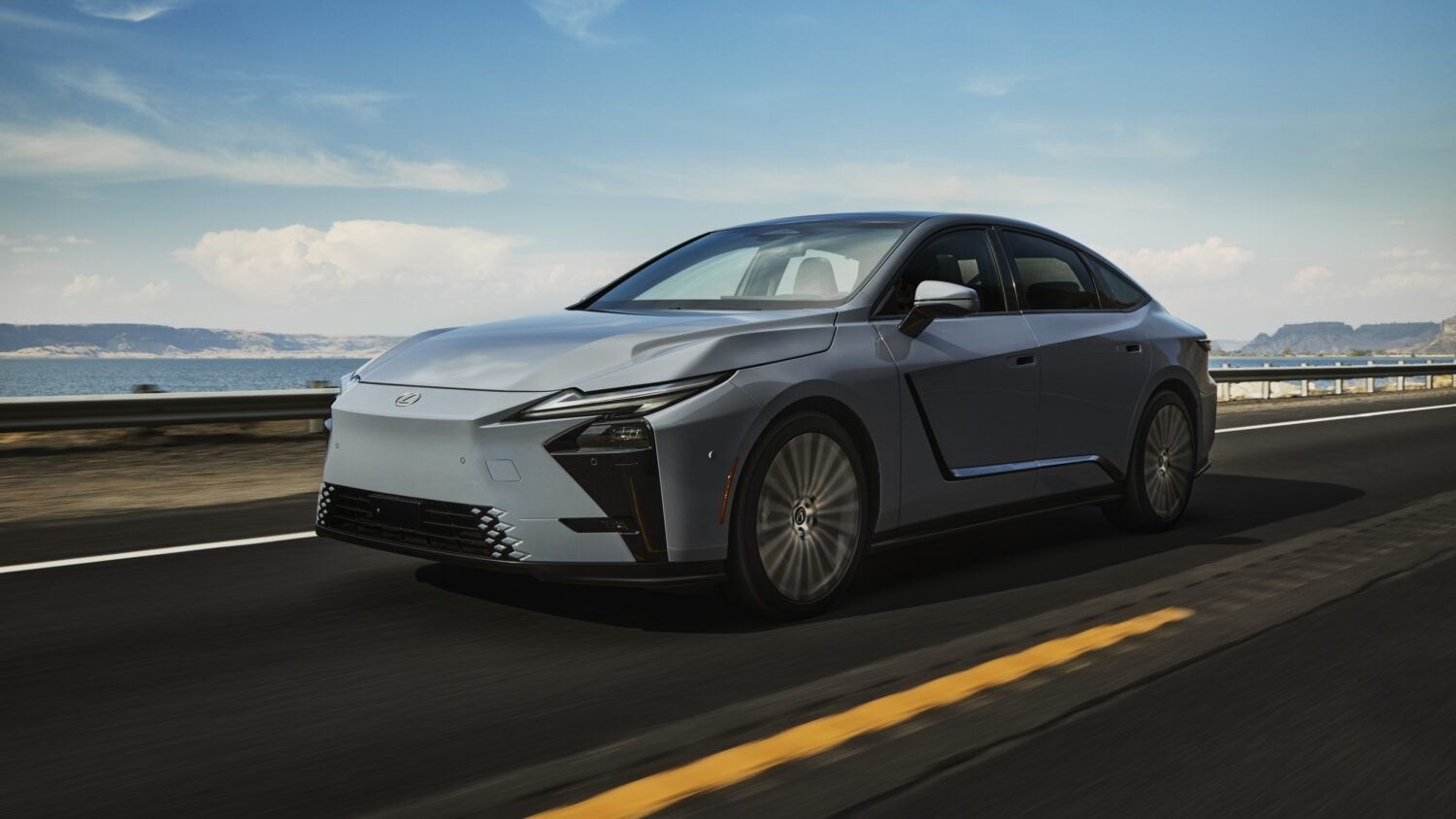 A light blue new Lexus ES 350e in Phoenix drives towards the viewer to the left ona seaside highway.