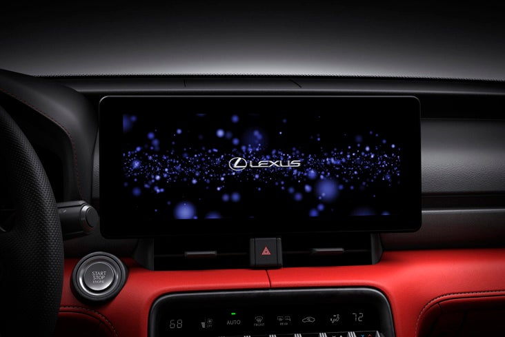 A close-up of the 10.3-inch high-resolution touchscreen in the Lexus IS 500. The screen displays the "LEXUS" logo over a blue stardust-themed background during its startup animation.