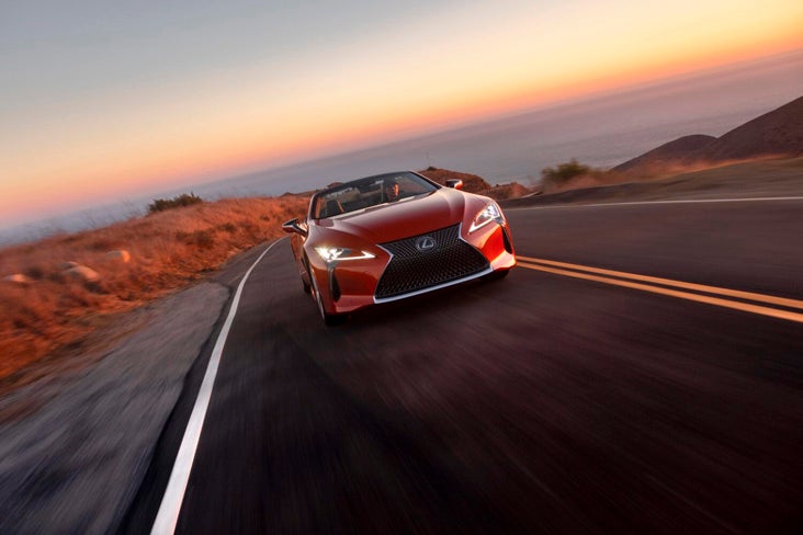 A red used Lexus LC in Phoenix drives towards the viewer, seen from a low angle, on a curvy desert road at sunset.