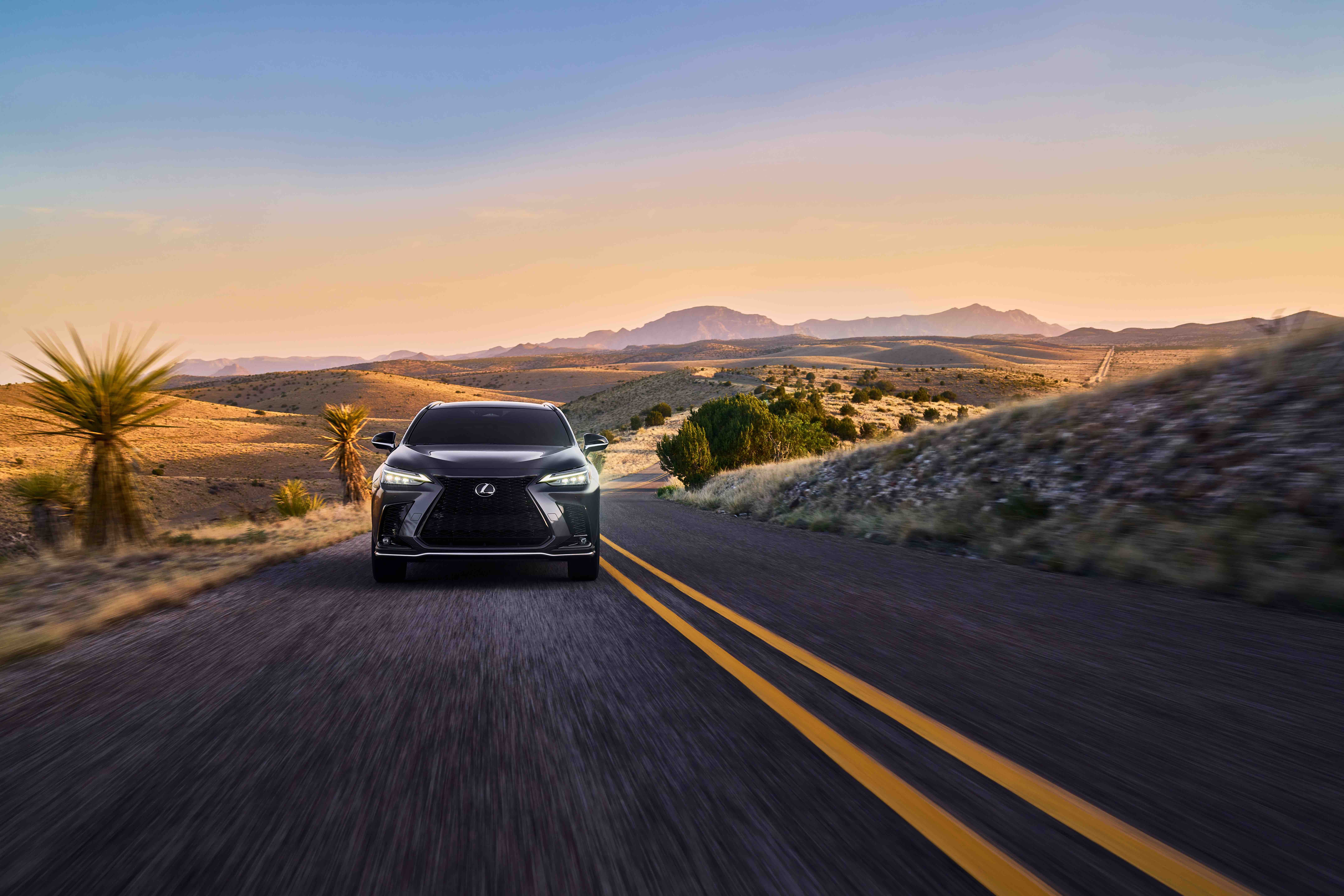 A grey used Lexus NX in Phoenix drives towards the viewer on a rural road through arid hills.